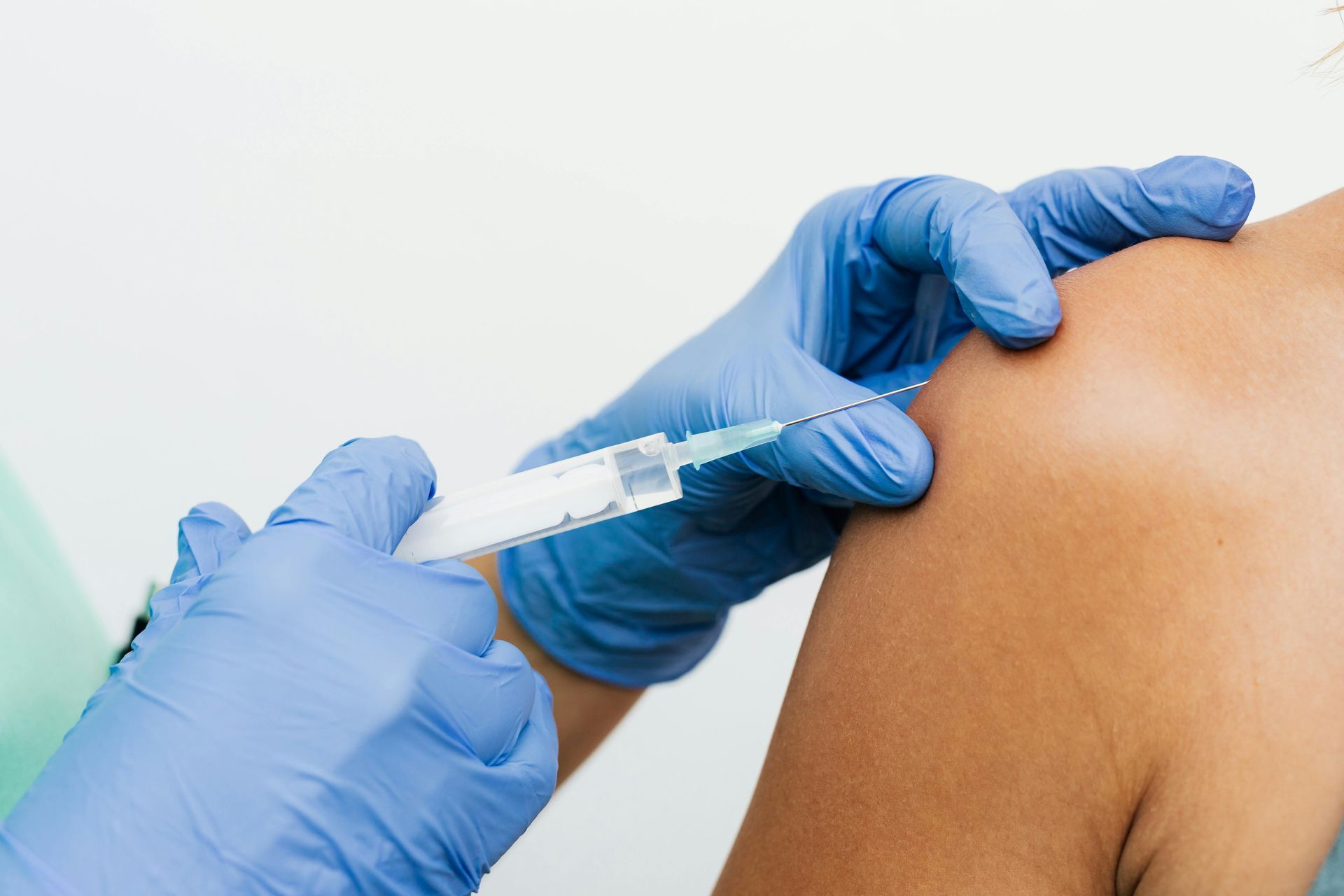 Gloved hand injecting vaccine into a person's shoulder.