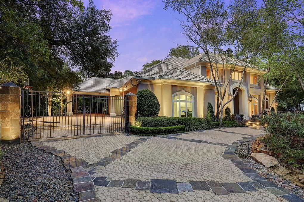 Large house with gated driveway and brick pavers. Evening setting with illuminated exterior.