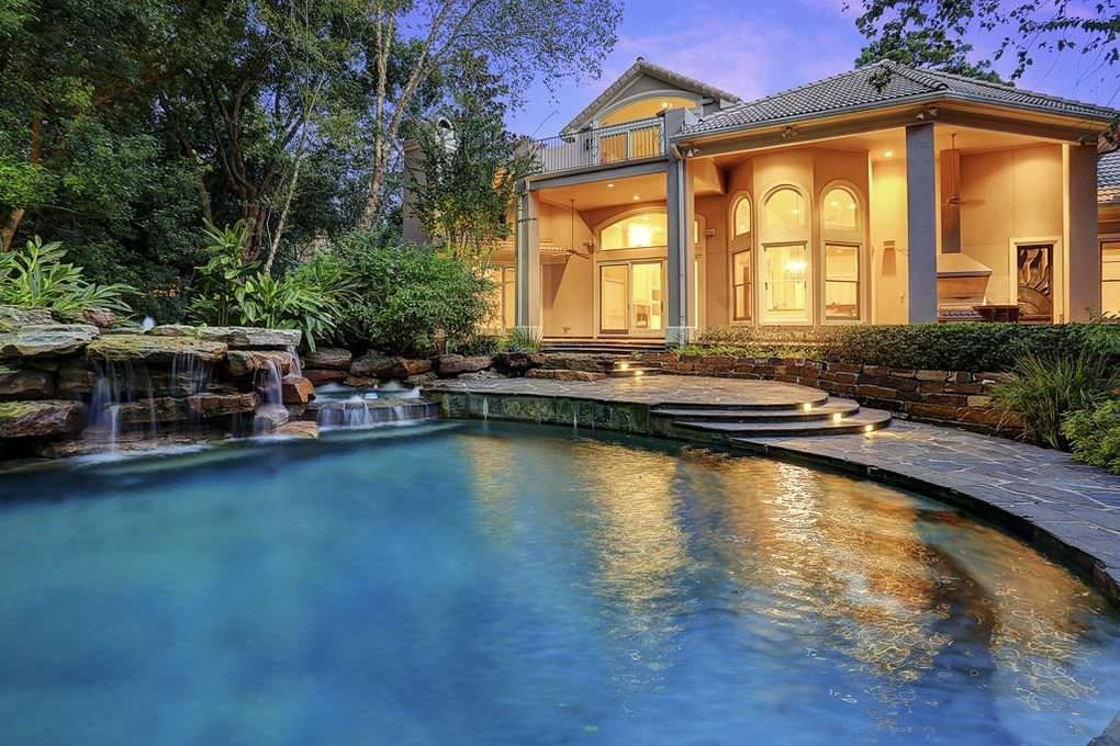 Luxury home with pool and waterfall, lit up at dusk.