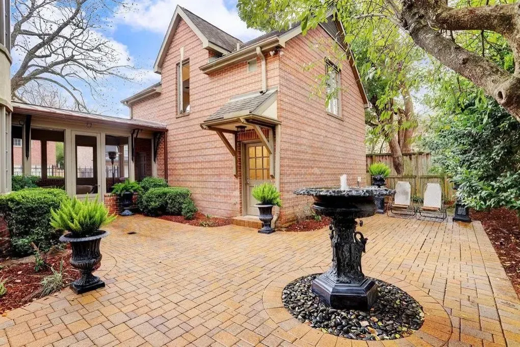 Brick patio with a fountain, building, and greenery.