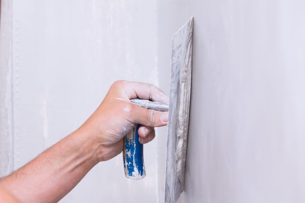 A Person is Plastering a Wall With a Metal Float — Clean Line Plastering in Taree, NSW