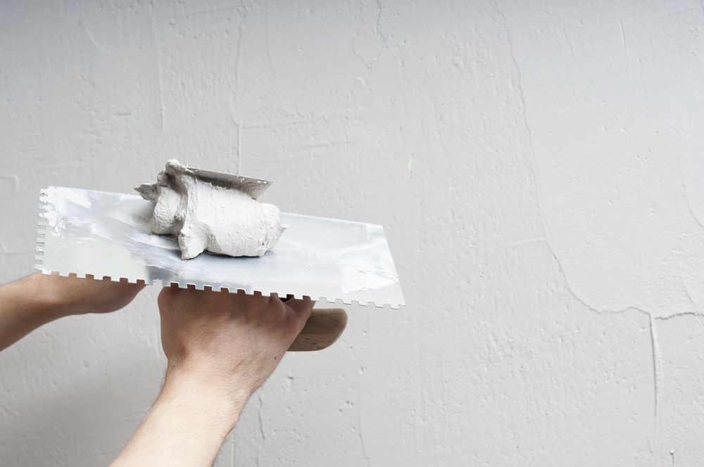 A Person Uses a Metal Float to Finish the Surface of a Plastered Wall — Clean Line Plastering in Pacific Palms, NSW