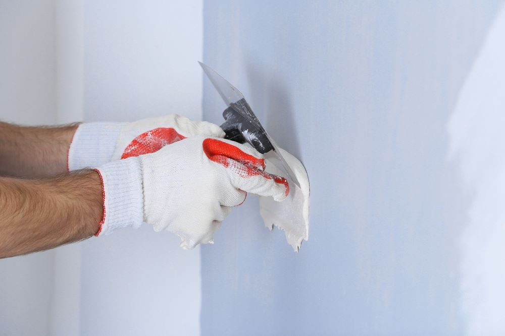 A Man is Plastering a Wall With a Metal Float — Clean Line Plastering in Taree, NSW