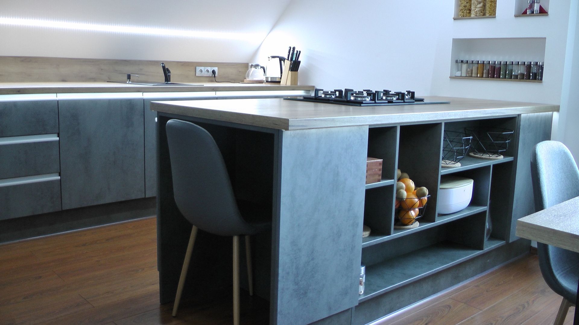Cuisine moderne avec placards gris, îlot central avec étagères et plaque de cuisson intégrée.