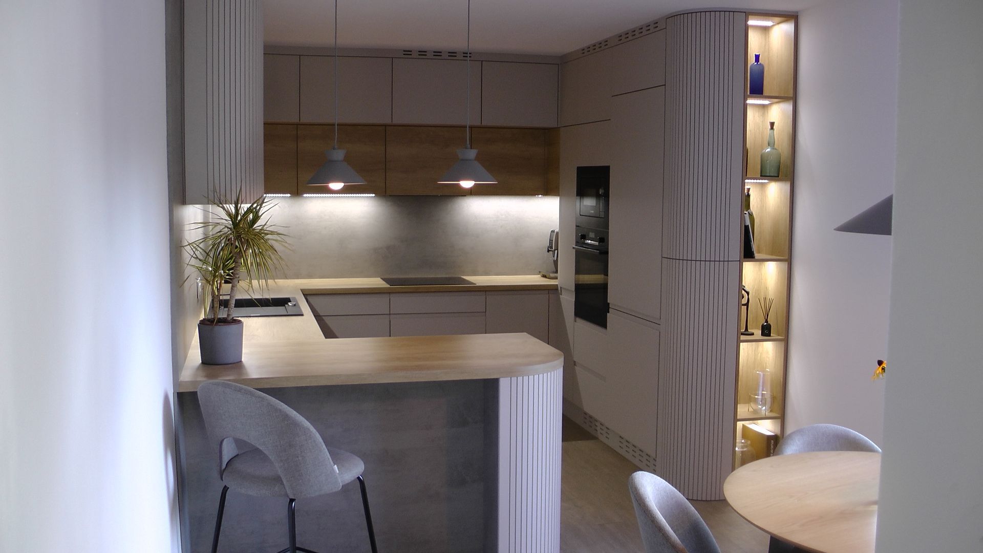 Petite cuisine moderne avec comptoirs en bois clair, armoires grises et un bar à petit-déjeuner incurvé.