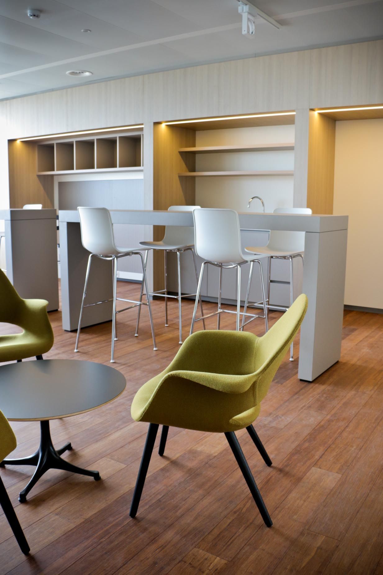 Intérieur d'un salon de bureau moderne avec sièges hauts, fauteuils jaunes et parquet.