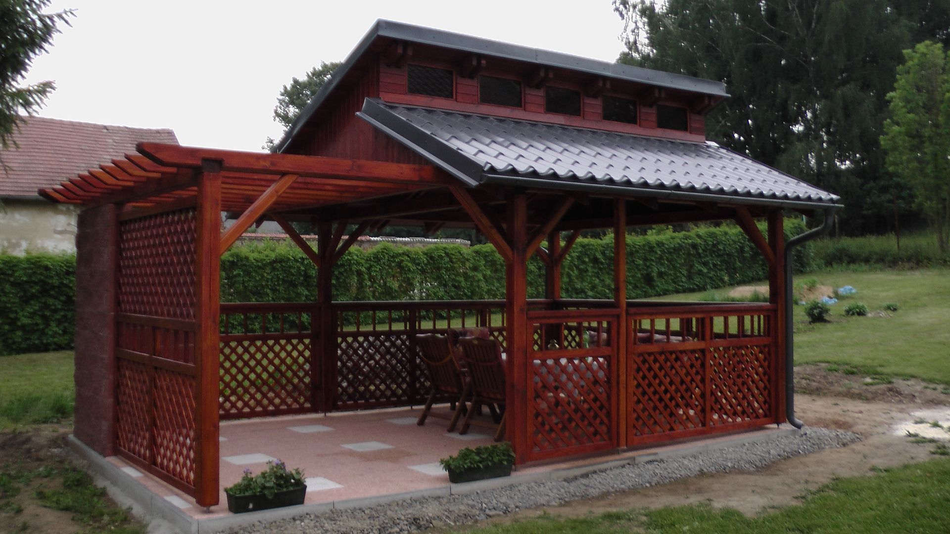 Un kiosque en bois rouge avec treillis et toit de tuiles dans une cour.