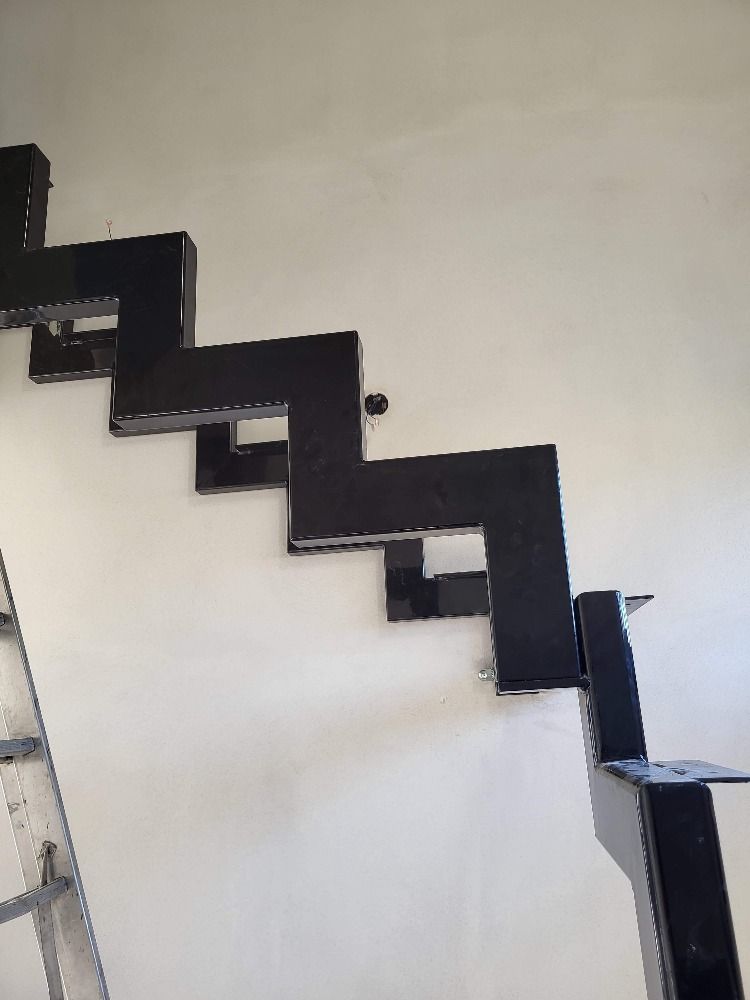 Escalier métallique noir en zigzag fixé à un mur blanc.