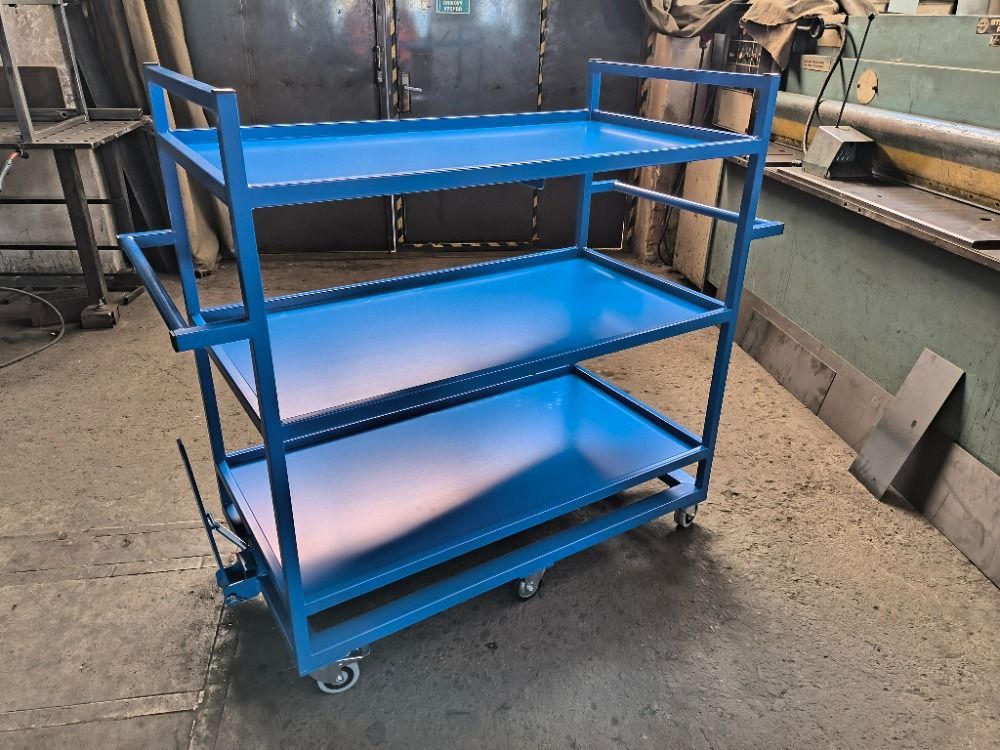 Chariot métallique bleu à trois niveaux, avec guidon et roues, dans un atelier.