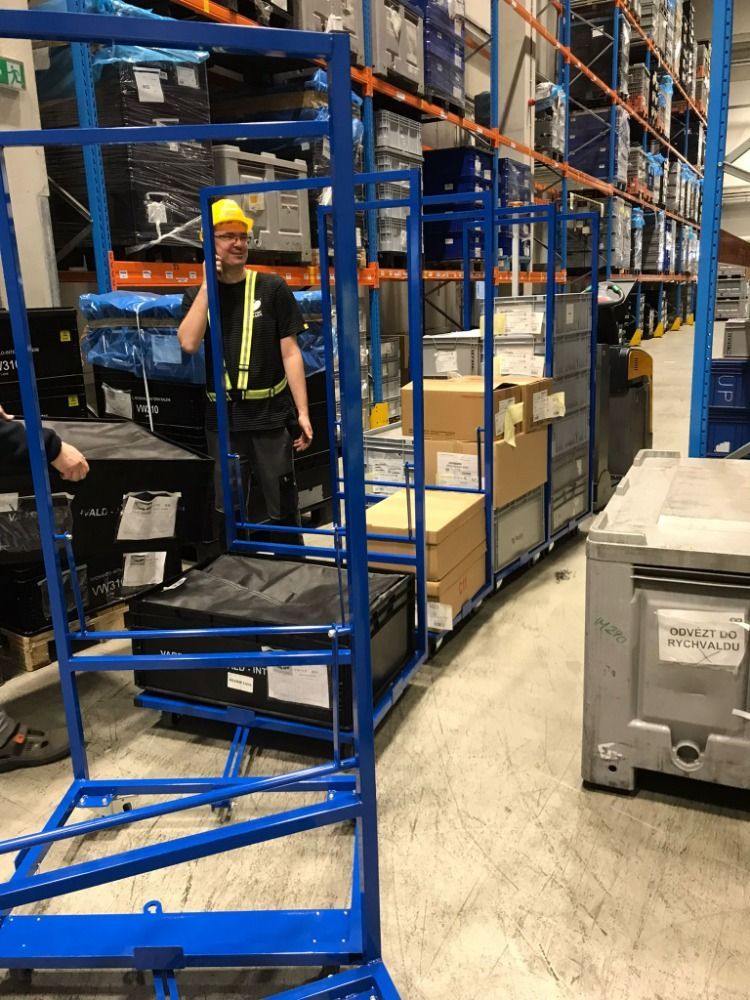 Chariot bleu transportant des cartons et des caisses dans un entrepôt, un employé au téléphone à proximité.