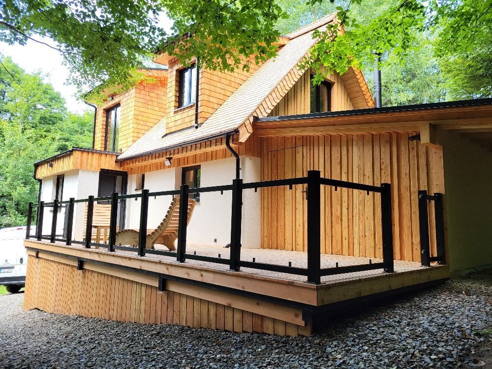 Cabane en bois avec terrasse et rambarde noire, entourée d'arbres.