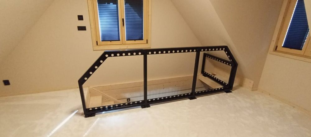 Une rambarde en métal noir dans une pièce avec un plafond mansardé et des fenêtres.