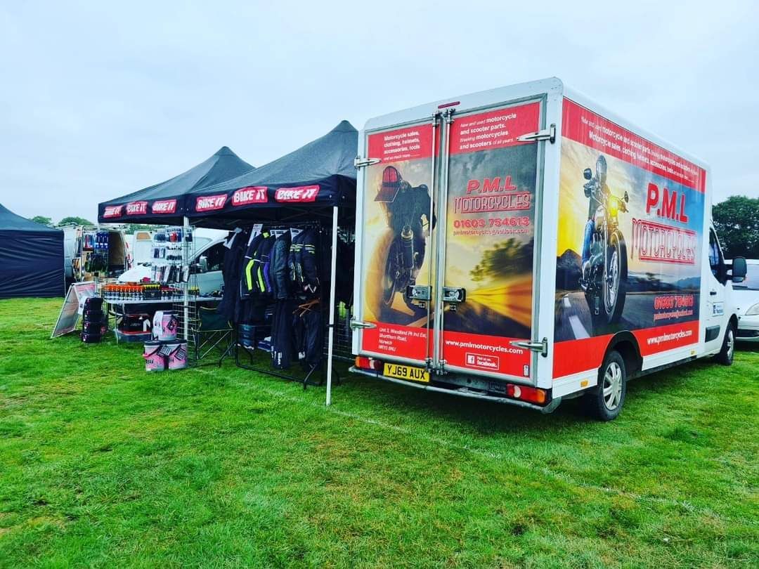 A motorcycle gear and accessories booth at an outdoor event. A branded truck and tent are set up on a grassy field.