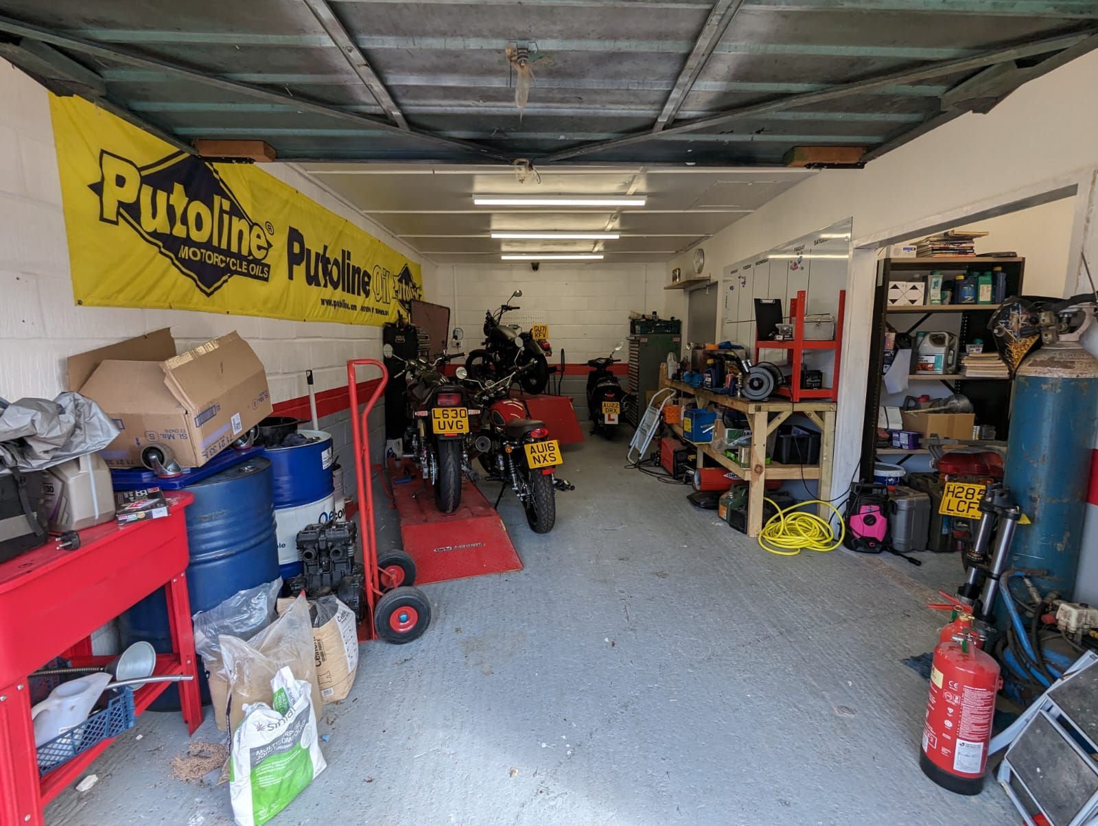 Garage interior, cluttered with motorcycles, tools, and equipment. Yellow banner on the wall.