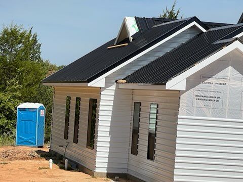 New house under construction with white siding, black roof, and a blue portable toilet.