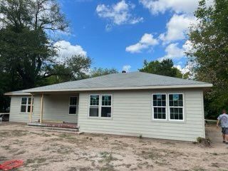 Light beige ranch house under construction with a clear blue sky, unfinished porch, and a person walking.