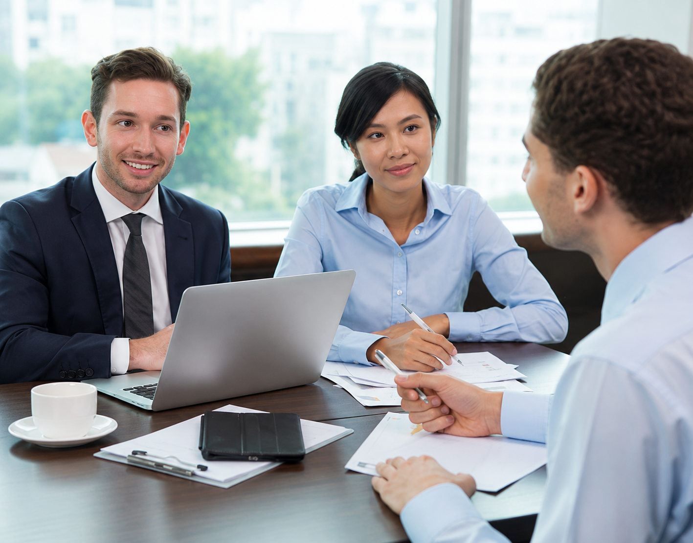 Three coworkers in a meeting around a laptop and papers in a bright office