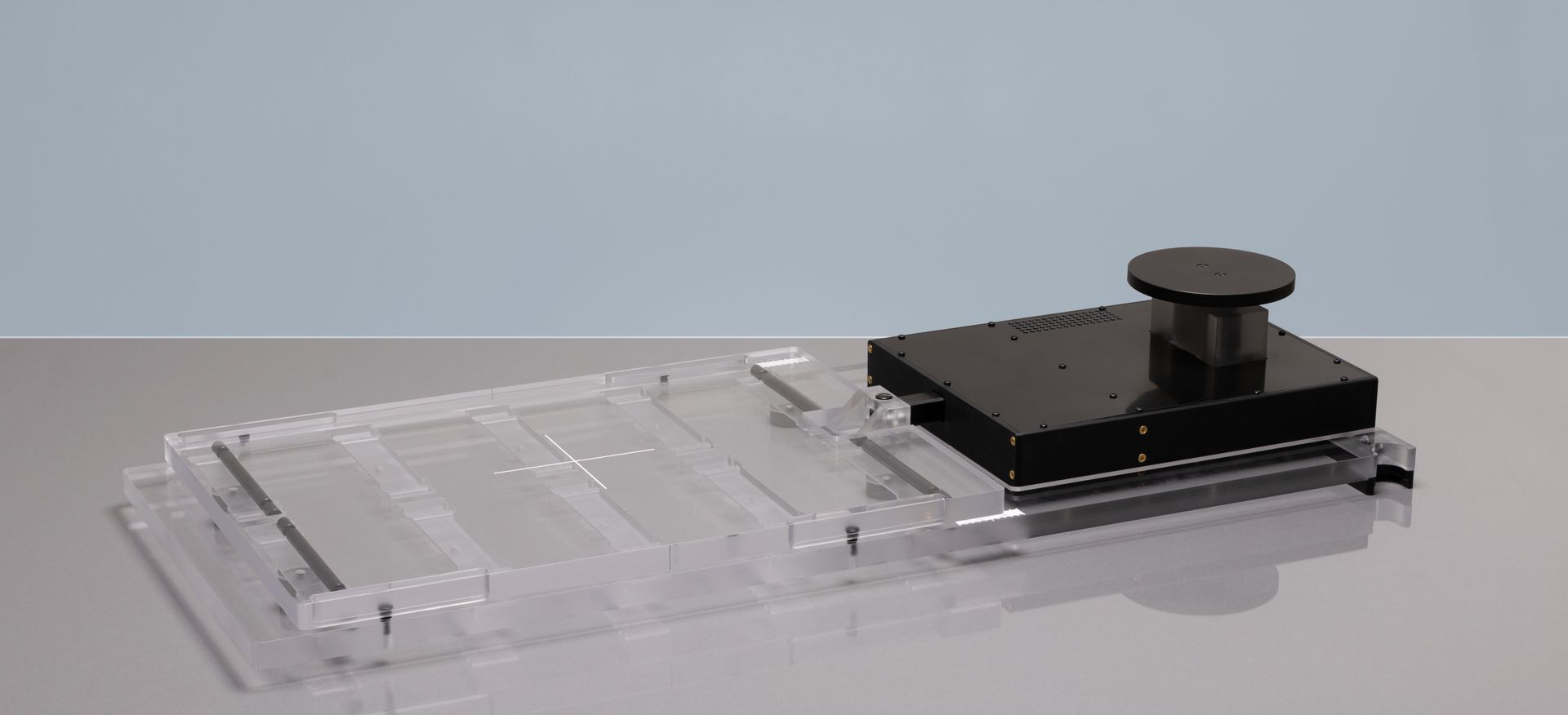 A clear plastic device with a black top and a push button on a gray surface.
