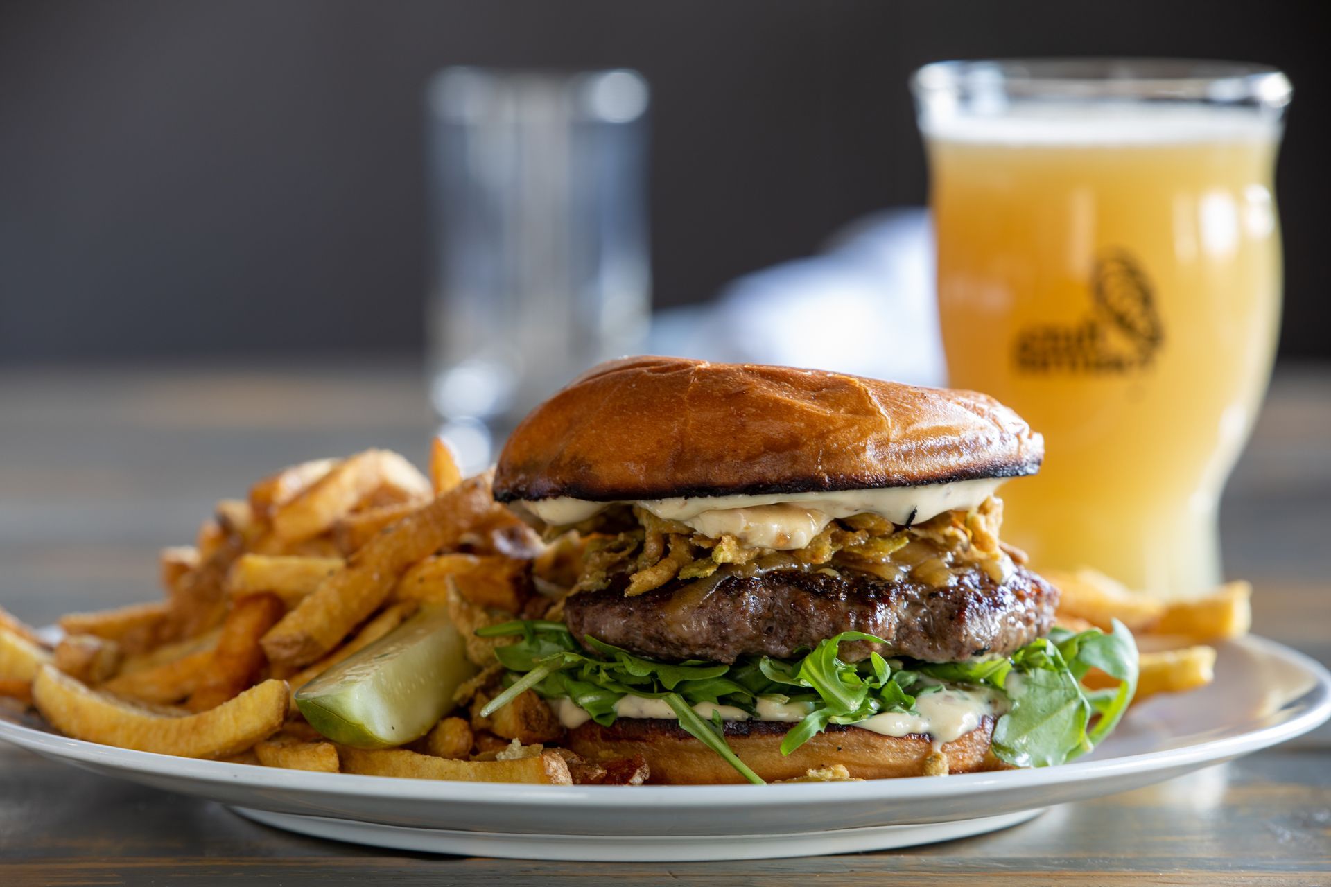 Burger with fries, a pickle, and beer on a plate.
