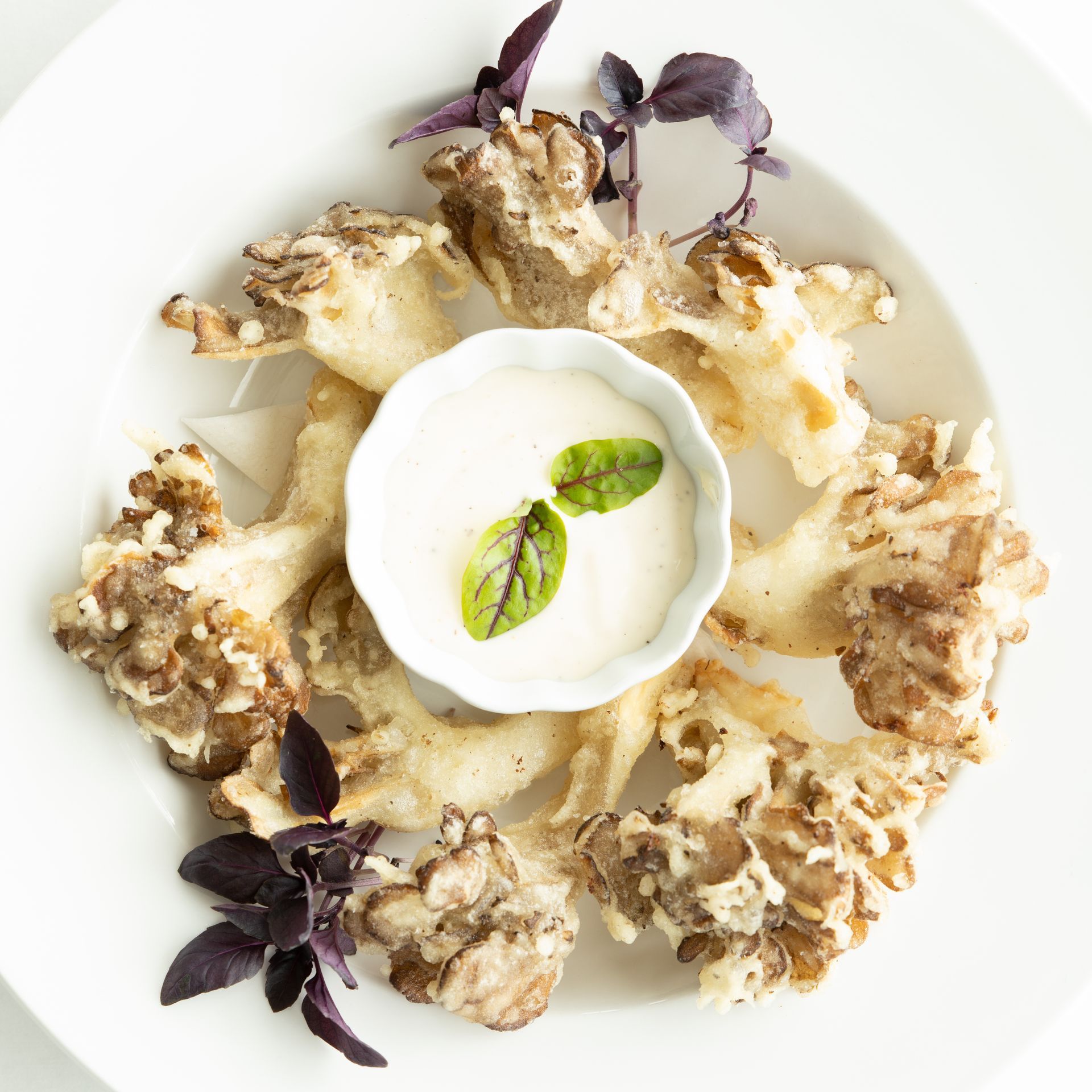 Tempura-battered mushrooms with dipping sauce on a white plate, garnished with basil.