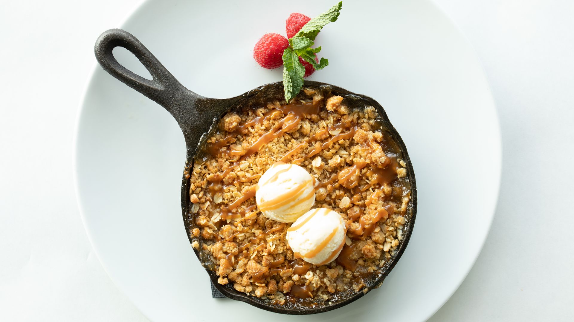 Apple crisp dessert in a skillet, topped with ice cream and berries on a white plate.