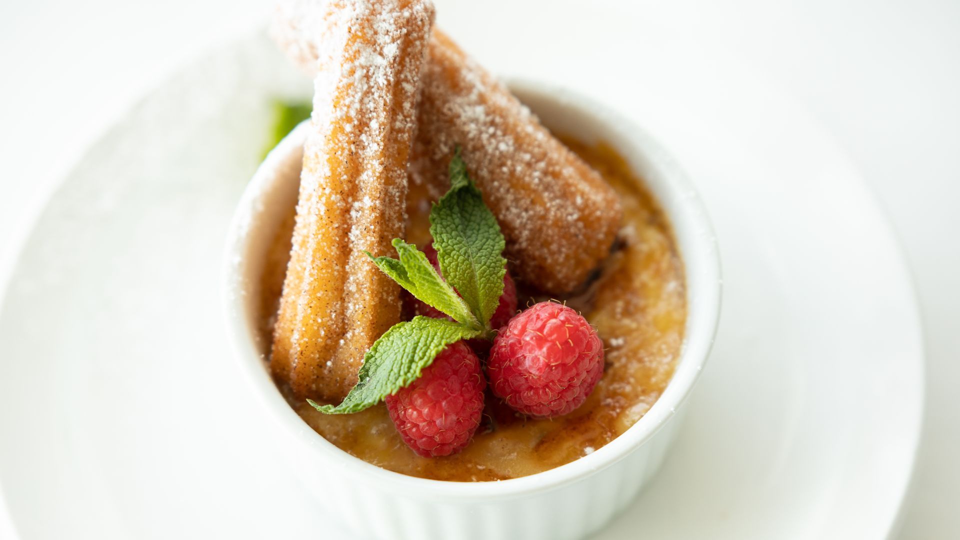Dessert of churros in a white ramekin with creme brulee, raspberries, and mint.