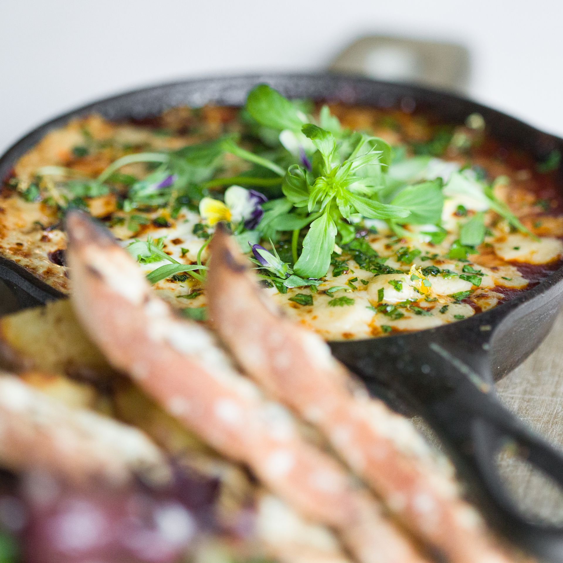 Skillet of baked dip topped with herbs and edible flowers, served with crispy bread.