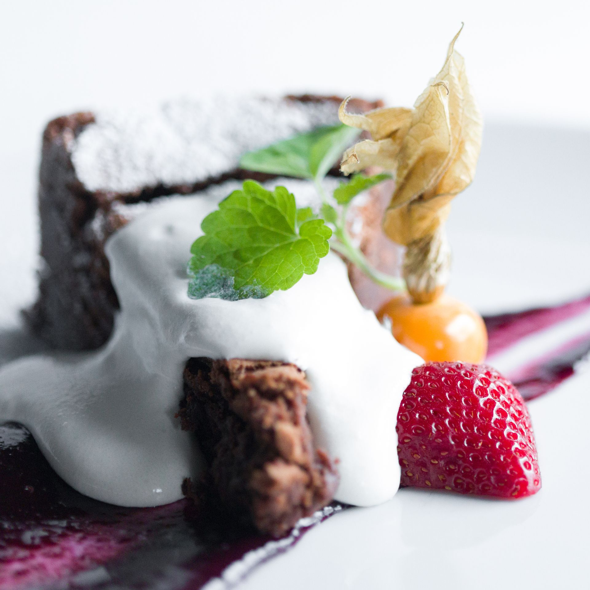 Chocolate dessert with whipped cream, strawberry, and a physalis berry.