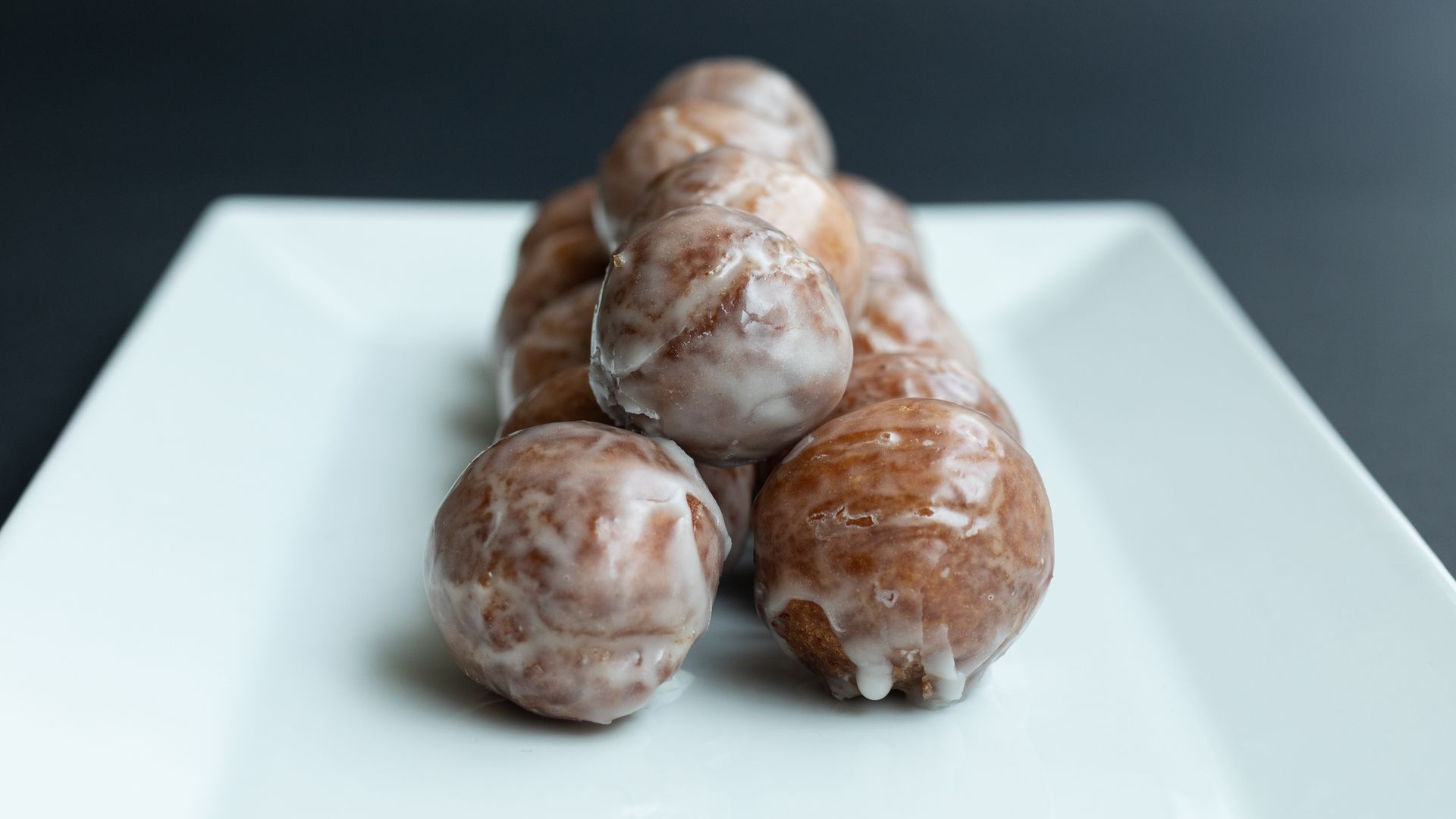 Glazed doughnuts stacked on a white plate, dark background.
