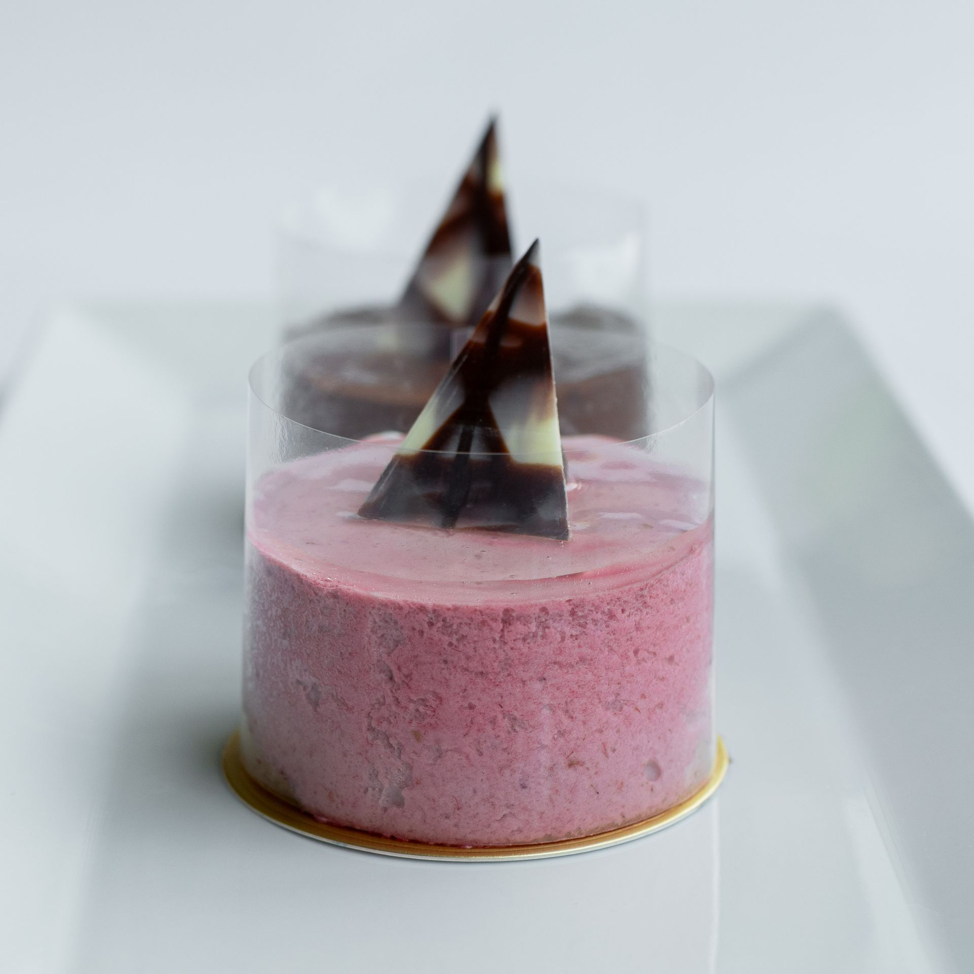 Two pink and brown mousse cakes, topped with chocolate triangles, on a white plate.