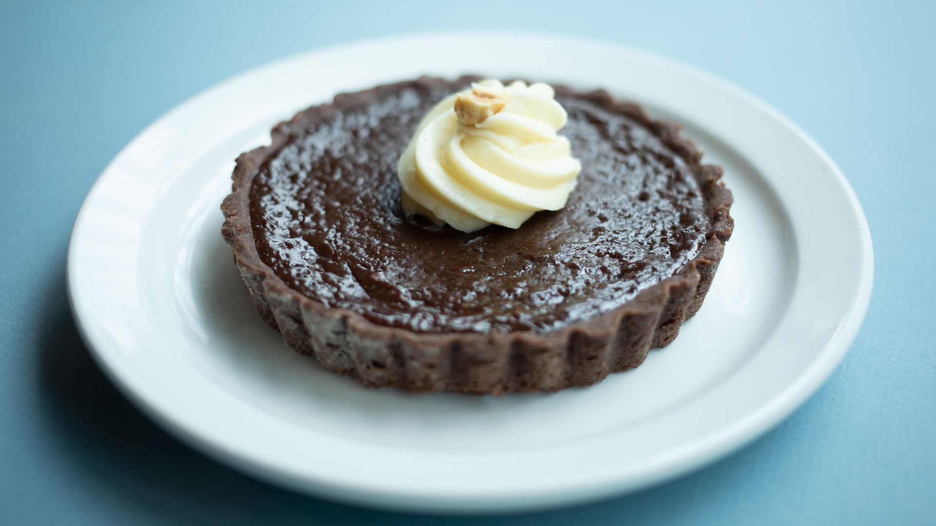 Chocolate tart with whipped cream topping on a white plate.