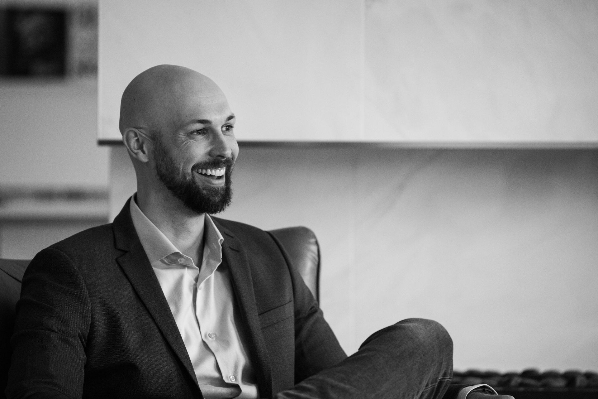 Man with a beard in a suit smiles, seated in a leather chair.