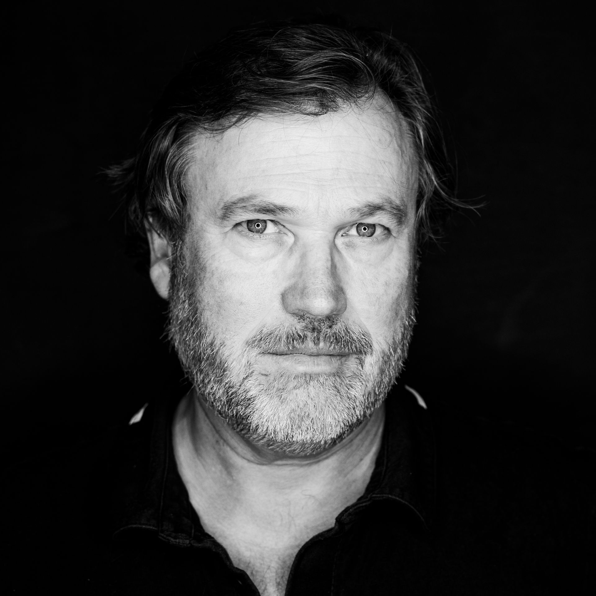 Man with a beard in a black shirt, looking directly at the camera. Black and white portrait.