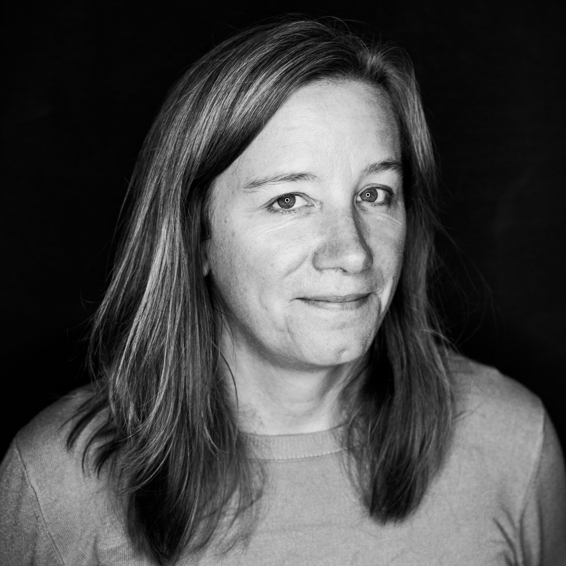 Woman with shoulder-length hair, smiling slightly, in a studio setting.