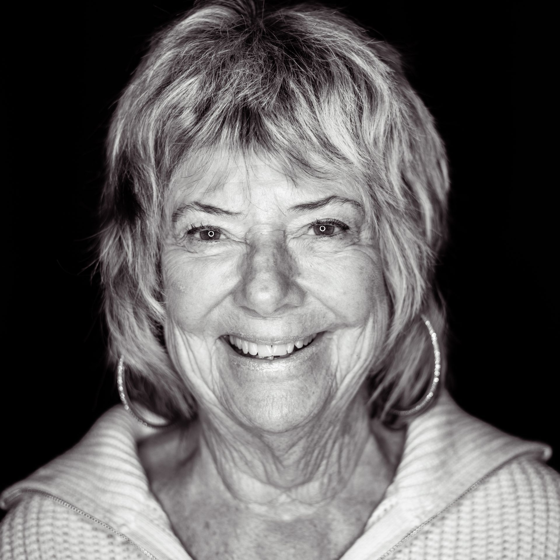 Smiling woman with short hair wearing hoop earrings and a zip-up sweater.