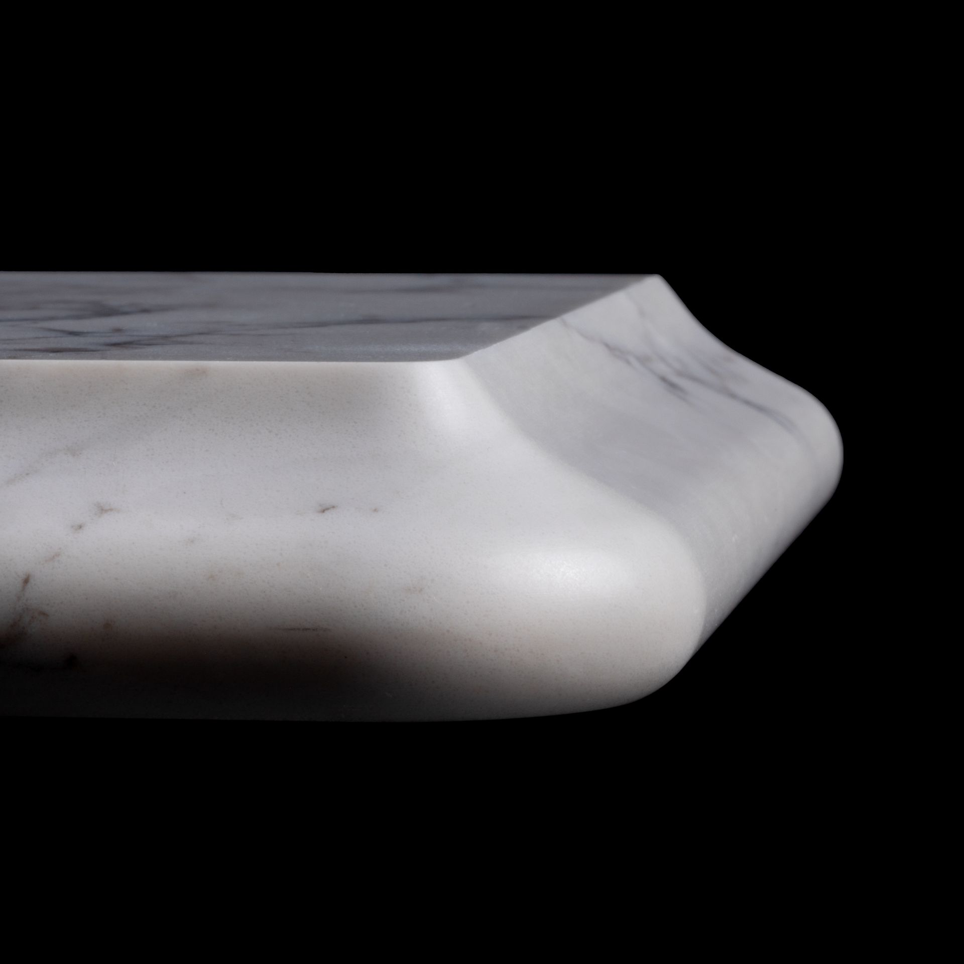 White marble countertop edge with rounded profile against a black background.