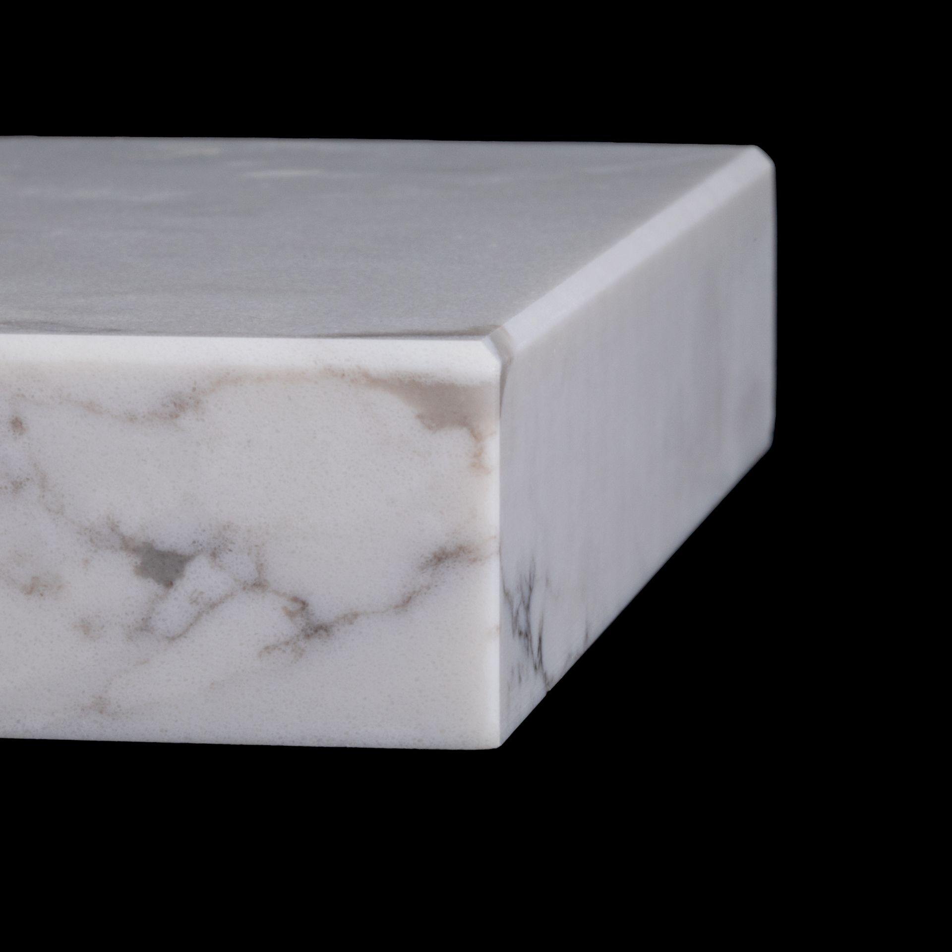 Close-up of a white marble countertop with gray veining and a slightly rounded edge, against a black background.