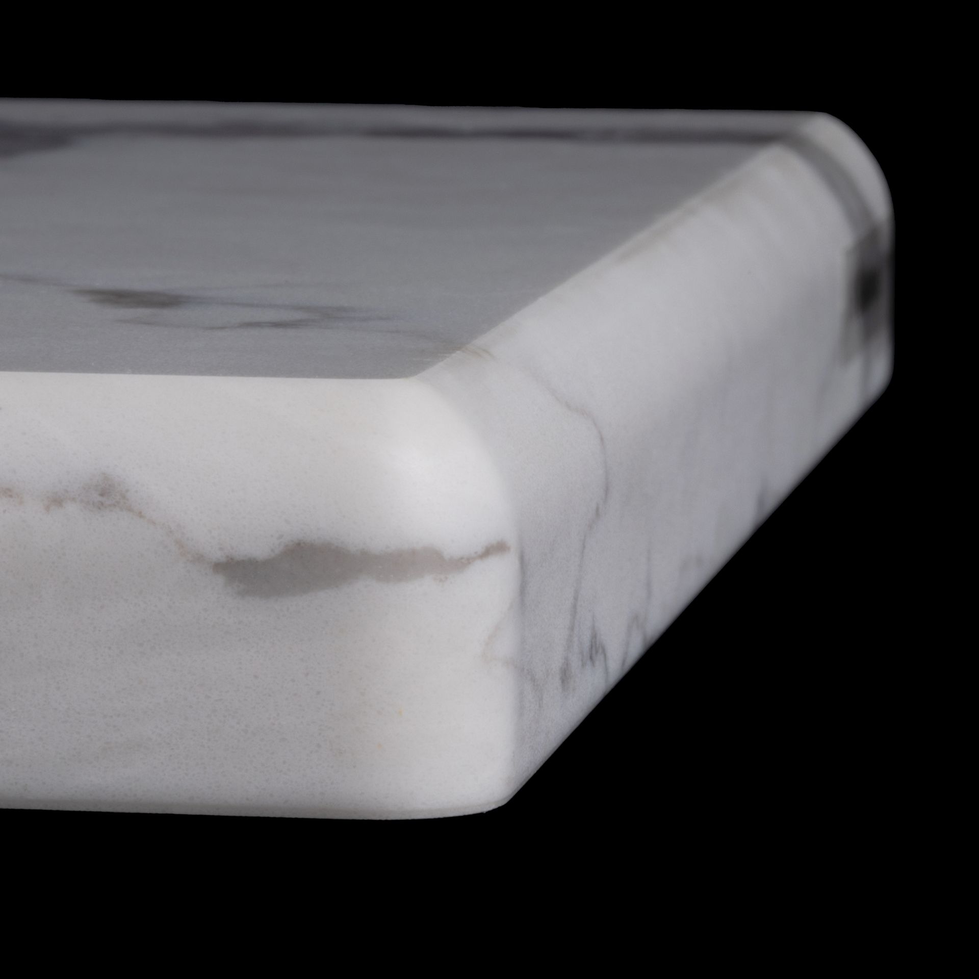 Close-up of a white marble countertop with a curved edge and gray veining.