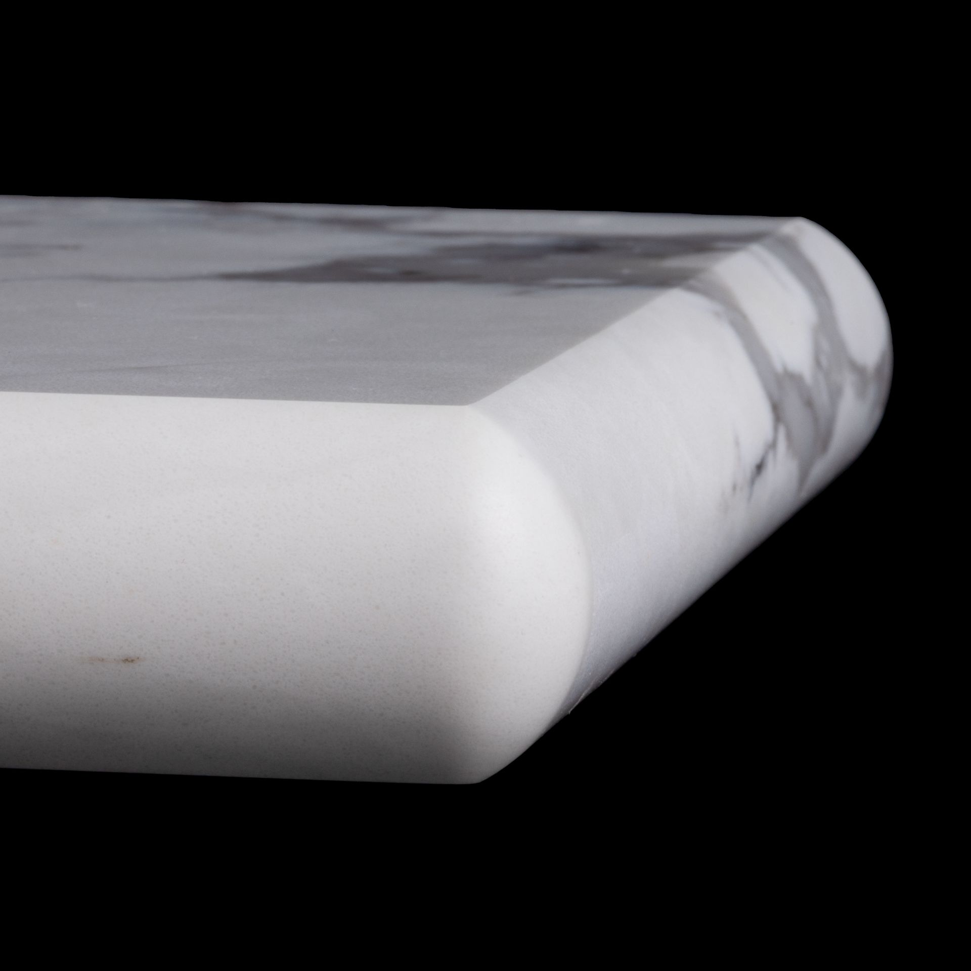 Close-up of a marble countertop edge. The edge is beveled and rounded with a white and gray pattern.