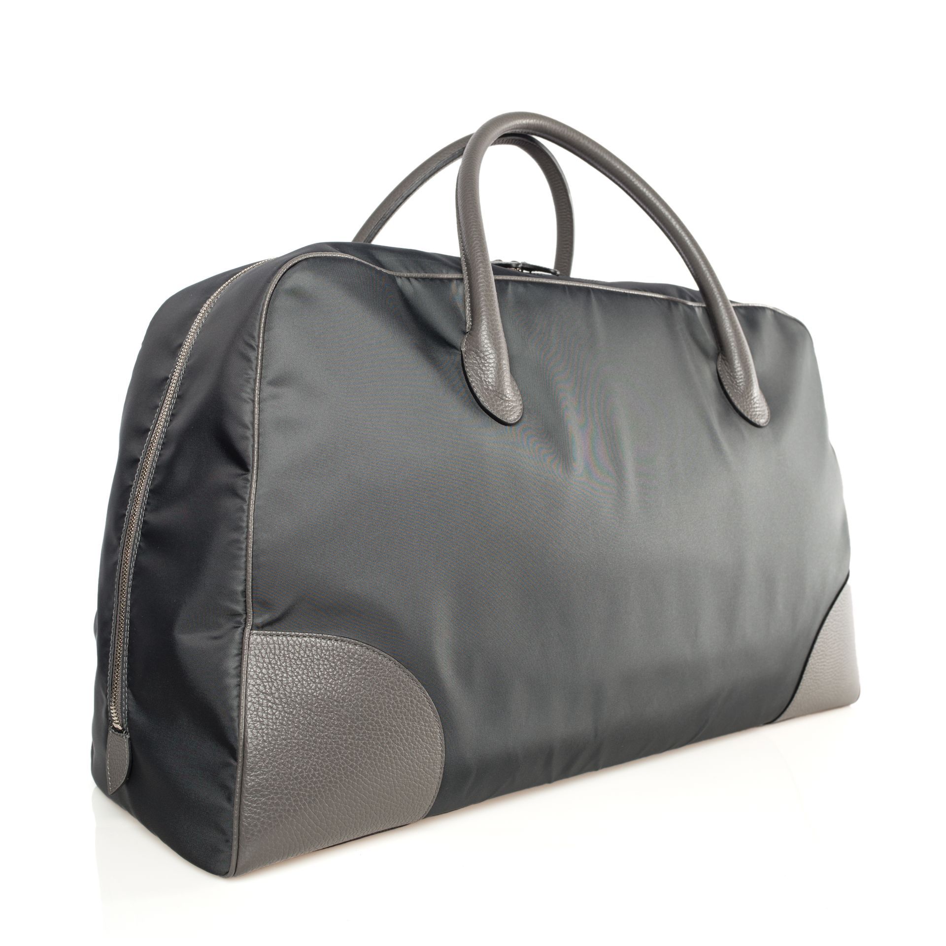 Black duffel bag with grey leather handles and trim, sitting on a white surface.