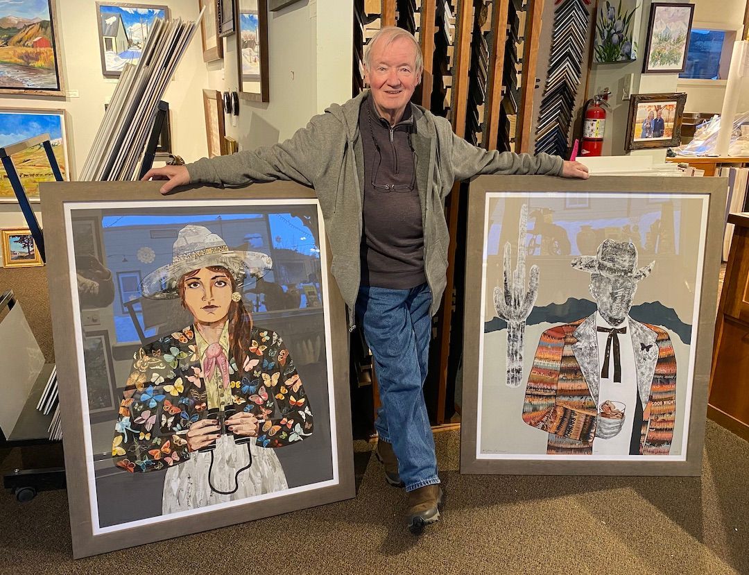 A man is holding two framed paintings in a room.