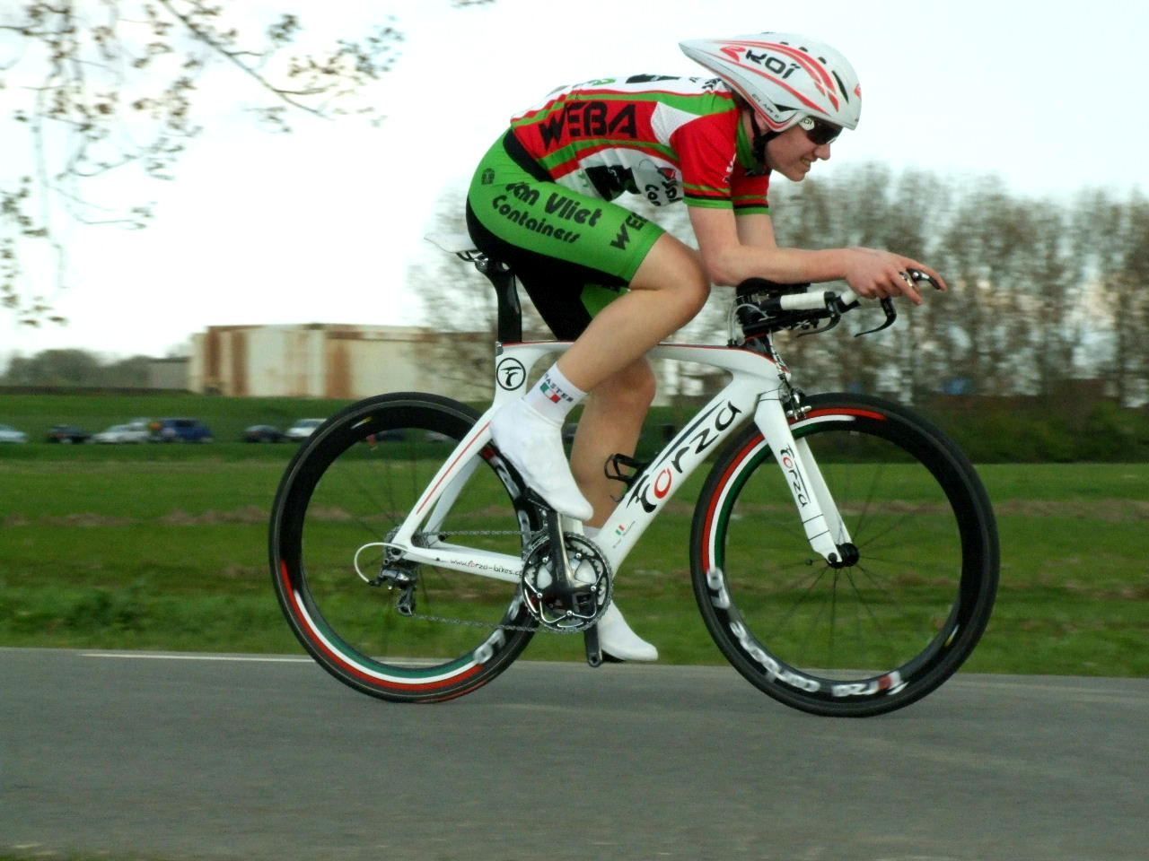 Een wielrenner in een wit-groen tenue op een witte fiets, racend op een weg.