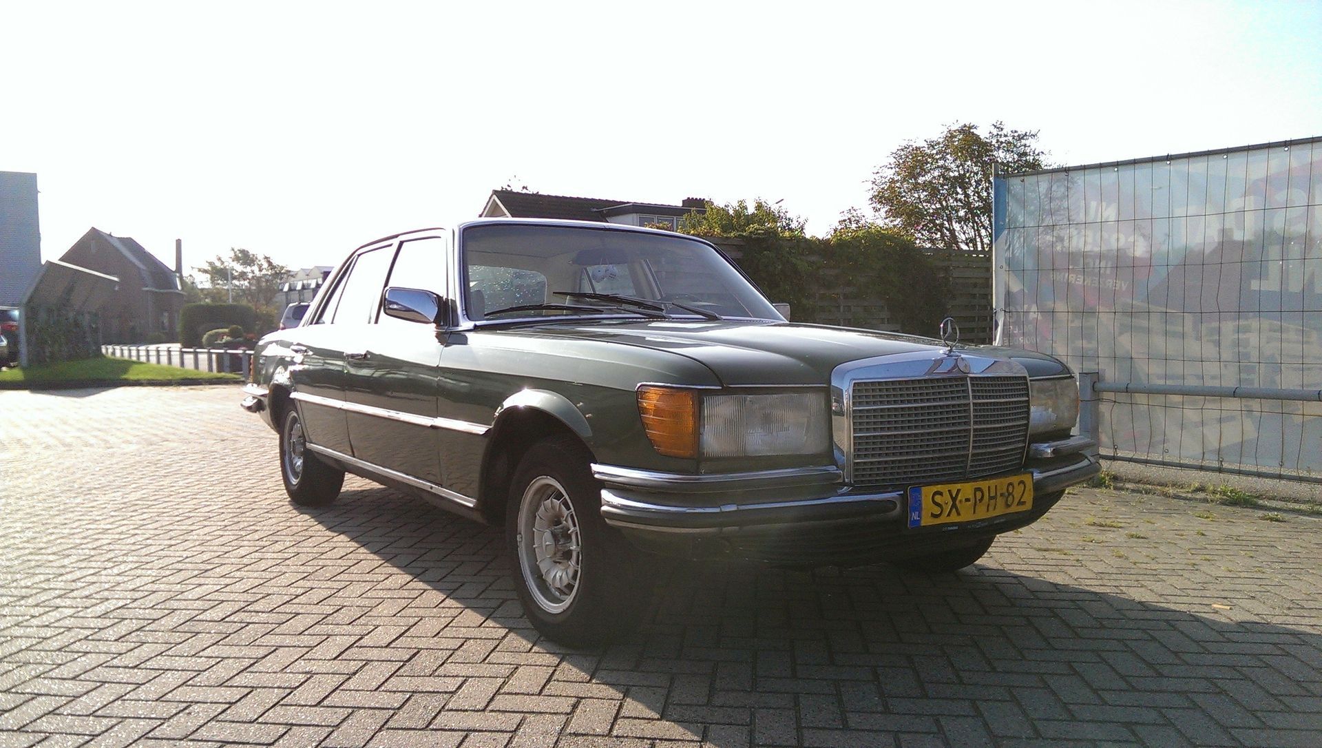 Groene Mercedes-Benz sedan geparkeerd op een bakstenen weg, zonnige dag. Nederlands kenteken.