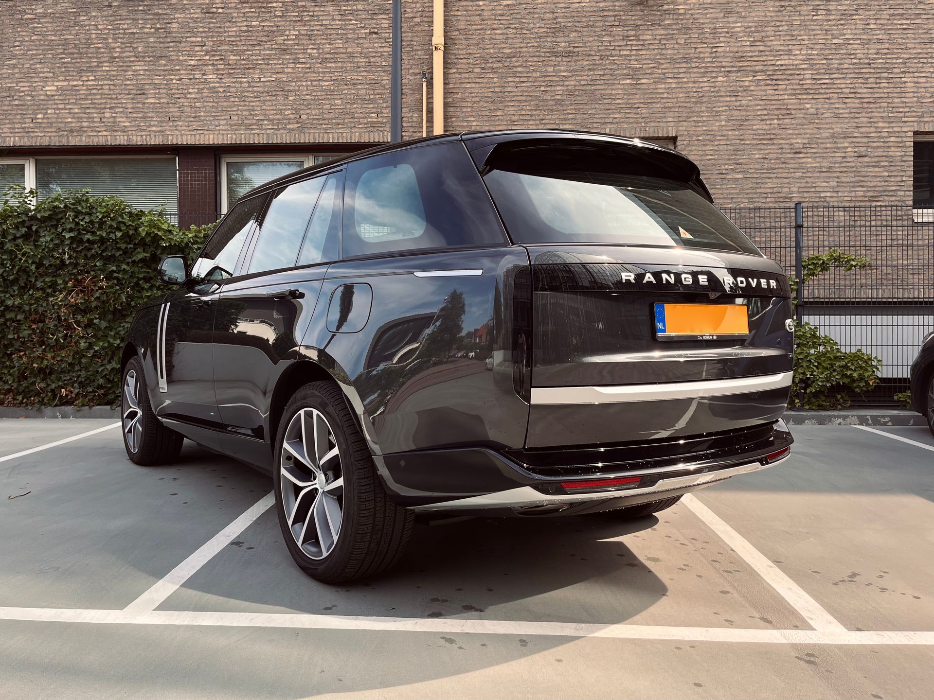 Een zwarte Range Rover SUV staat geparkeerd op een parkeerplaats buiten, vlakbij een bakstenen gebouw.