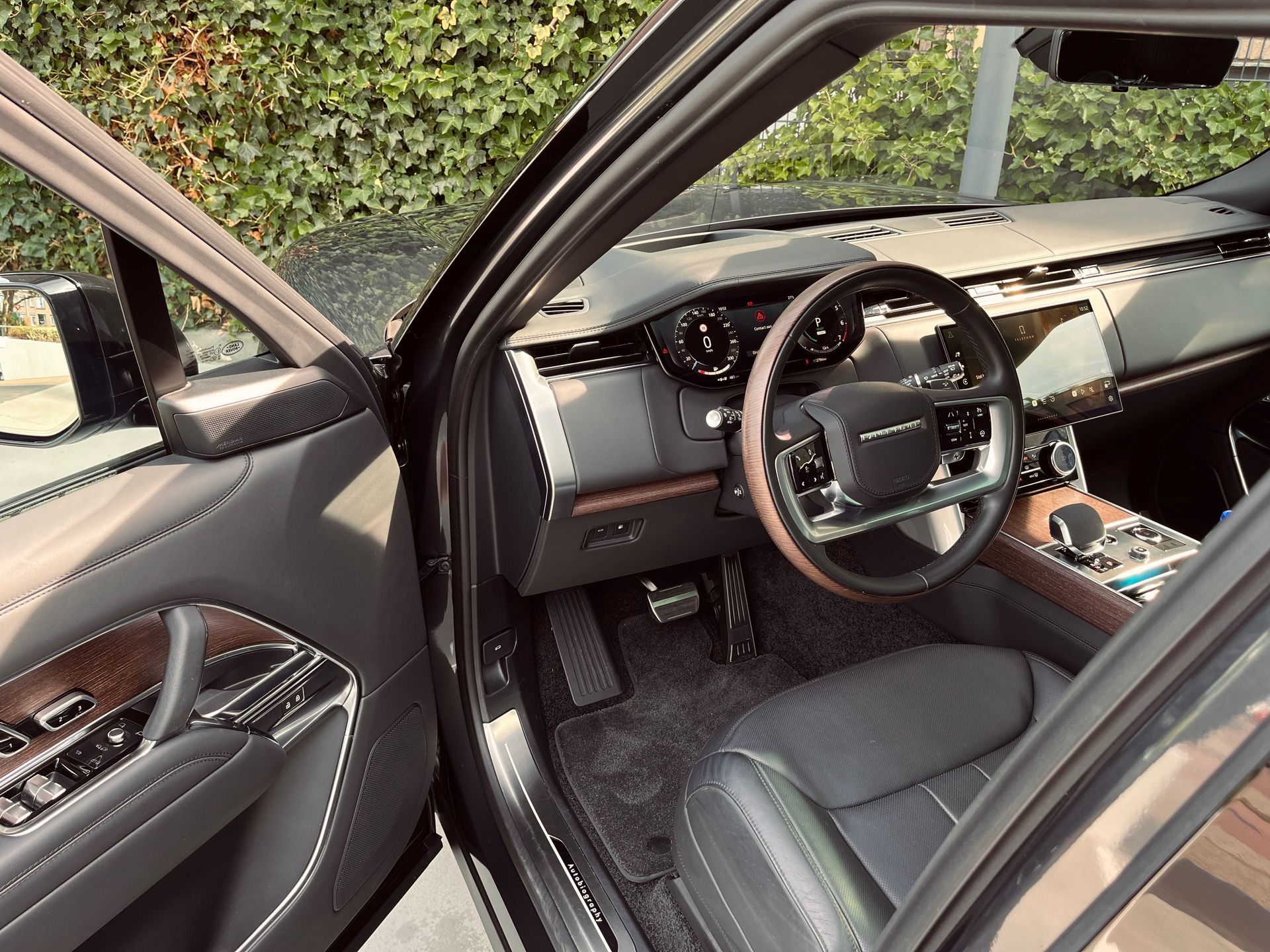 Interieurfoto van een zwarte Range Rover SUV met een open deur, waarop het dashboard, het stuurwiel en de voorstoel te zien zijn.