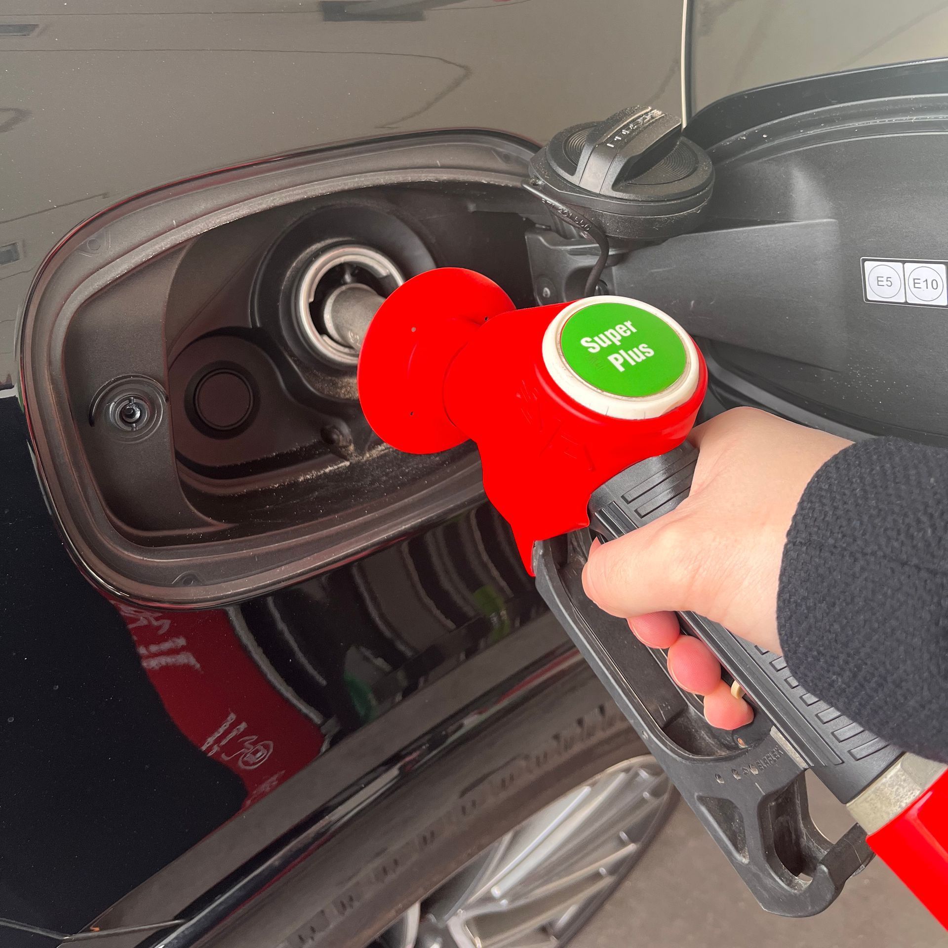 Brandstofpompmondstuk in de benzinetank van een auto. Hand houdt een rood mondstuk vast met een groen 