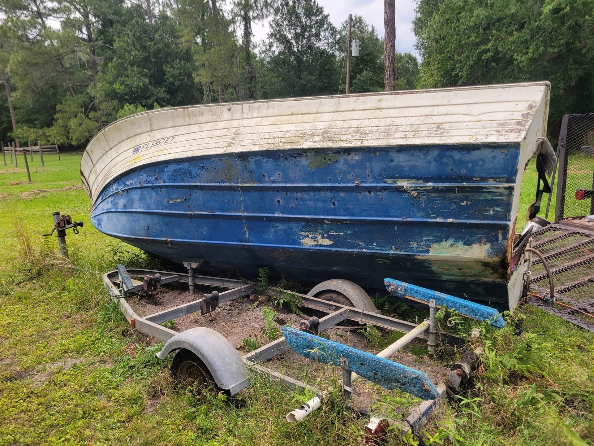 A blue and white boat is sitting on a trailer in a grassy field.