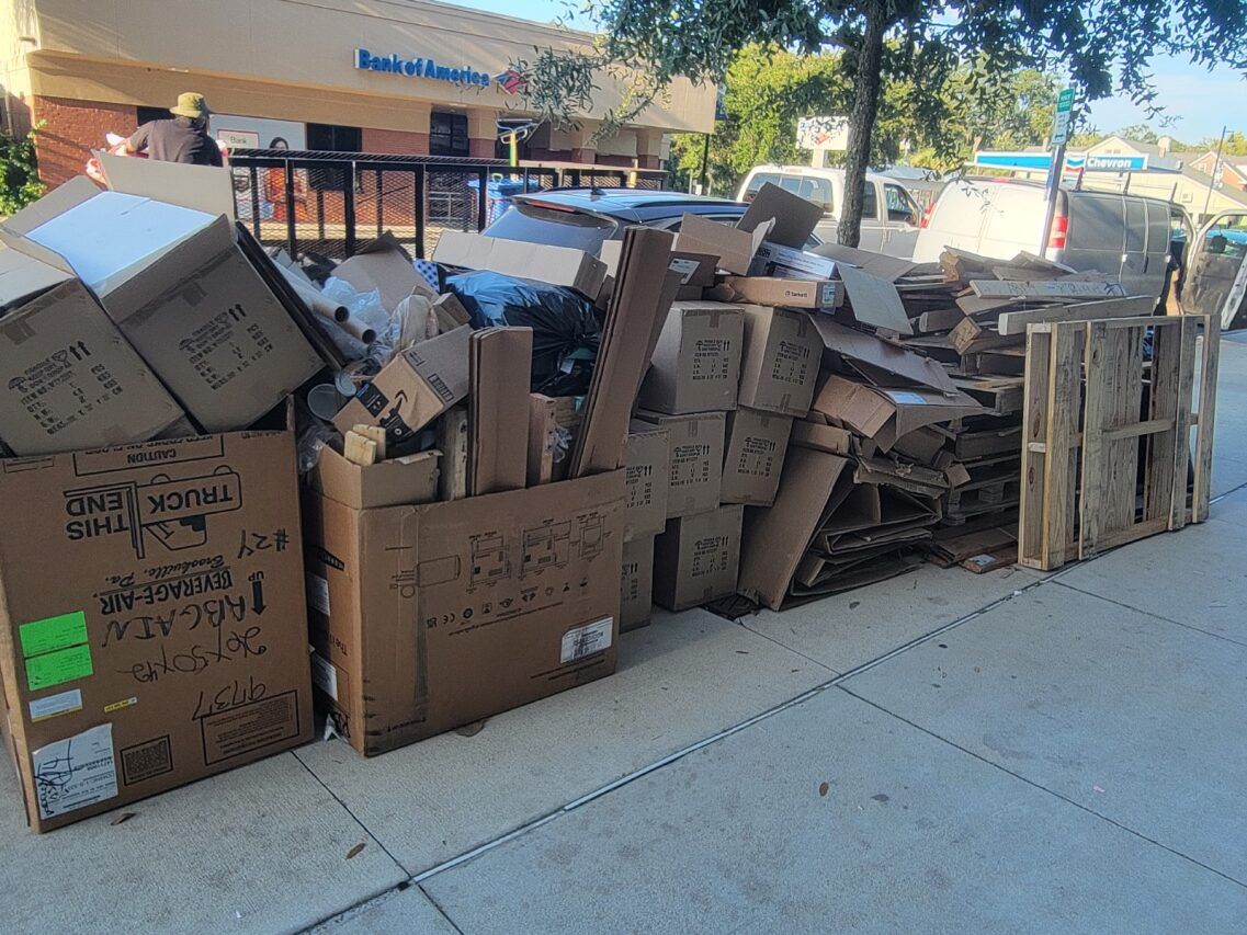 Pile of cardboard boxes, wood pallets, and debris on a sidewalk in front of a building.