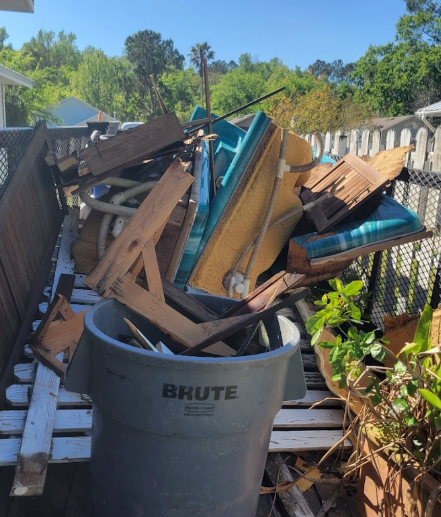 A gray trash can overflowing with construction debris on a wooden deck.