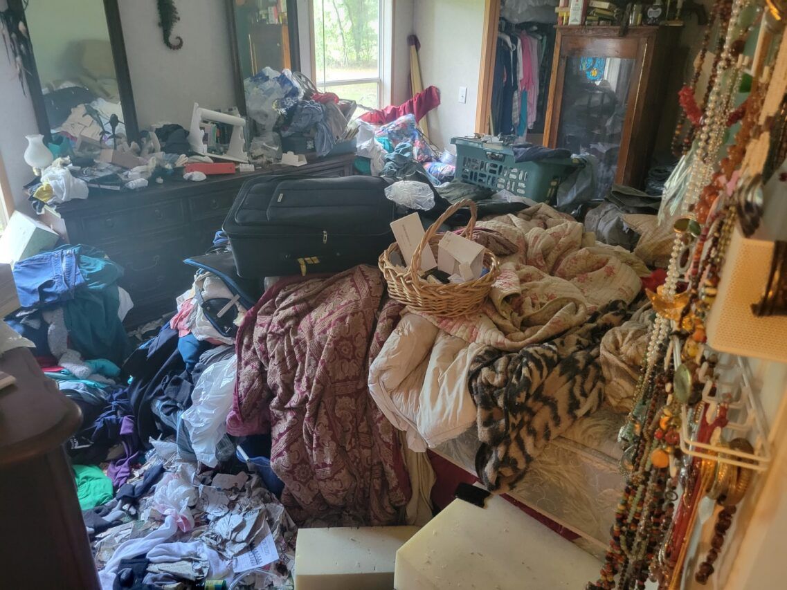 A bedroom filled with lots of clothes and a suitcase.